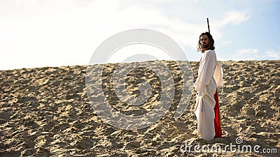 Hermit with staff walking in desert looking to camera, asceticism and fasting Stock Photo