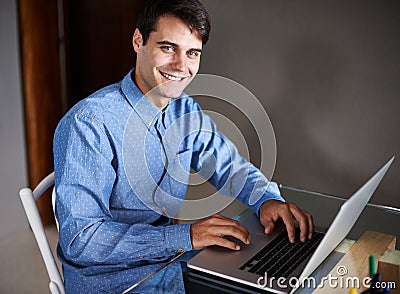 Hes a go-getter. Portrait of a confident young businessman sitting with a laptop at his desk. Editorial Stock Photo