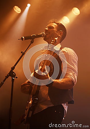 Hes the perfect front man. A young man singing and playing guitar on stage. Stock Photo