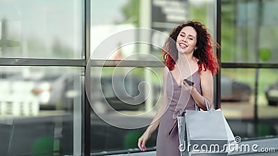 Het charmante roodkopmeisje met smartphone die graag wandelen tegen de achtergrond van klein glas koopt stock footage Het charmante roodkopmeisje met smartphone die graag wandelen tegen de achtergrond van klein glas koopt stock footage