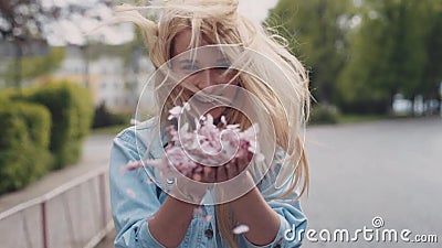 Het Europese jonge blonde aantrekkelijke meisje beweegt zich onderaan het park, dan draait zij en werpt de bloemblaadjes van kers stock video Het Europese jonge blonde aantrekkelijke meisje beweegt zich onderaan het park, dan draait zij en werpt de bloemblaadjes van kers stock video