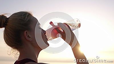 Het zijaanzicht van mooi meisje in sportkleren opent haar roze gekleurd sportfles en drinkwater dichtbij na training stock footage Het zijaanzicht van mooi meisje in sportkleren opent haar roze gekleurd sportfles en drinkwater dichtbij na training stock footage