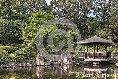 Hexagonal Gazebo Ukimido in the central pond of Mejiro Garden where carp swim and which is surrounded by large flat stones under Stock Photo