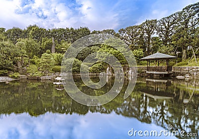 Hexagonal Gazebo Ukimido in the central pond of Mejiro Garden where ducks are resting and which is surrounded by large rocks and Stock Photo