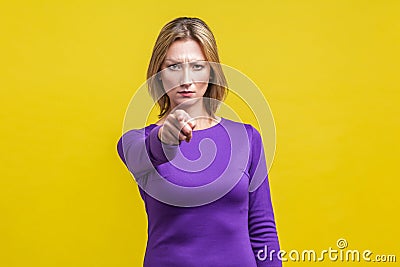 Hey you! Portrait of serious bossy woman in tight purple dress pointing at camera. indoor studio shot on yellow Stock Photo