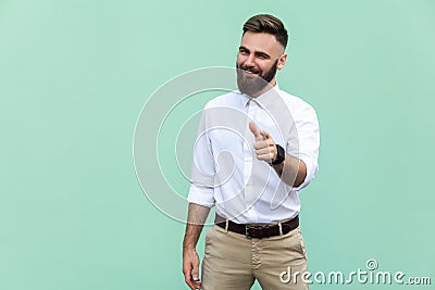 Hey you! Young adult bearded man, pointing finger and looking at camera. On light green background. Indoor Stock Photo