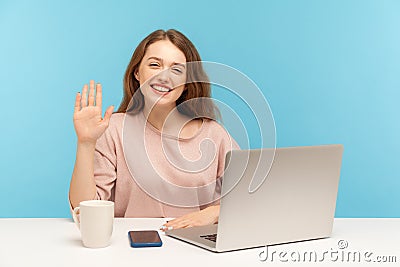 Hi! Friendly beautiful young woman employee waving hand gesturing hello while sitting at workplace, secretary on reception Stock Photo