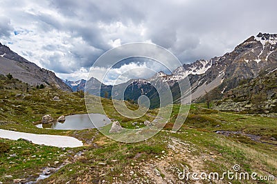 High altitude alpine pond in extrem terrain rocky landscape once covered by glaciers. Dramatic stormy sky and snowcapped mountain Stock Photo