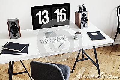 High angle of a desk with a computer, notebooks, speakers and keyboard next to a chair in a home office interior. Real photo Stock Photo