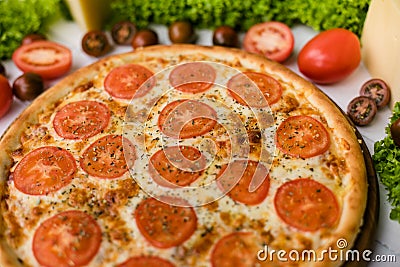 High angle view of fresh pizza on white wooden table surrounded by salad, vegetables and cheese Stock Photo