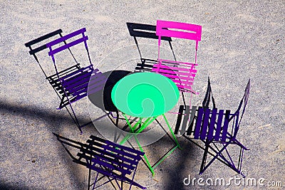 High angle view on green round table with four wood pink and purple folding chairs outdoor in bright sunlight Stock Photo