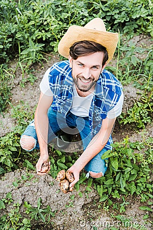 high angle view of handsome farmer squatting in field at farm and holding Stock Photo