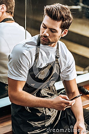 High angle view of handsome young hairstylist using smartphone and looking away Stock Photo