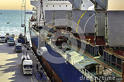 High angle view of huge cargo ship discharge steel at port terminal. Ship crane lift steel coil put down on truck for delivery Stock Photo