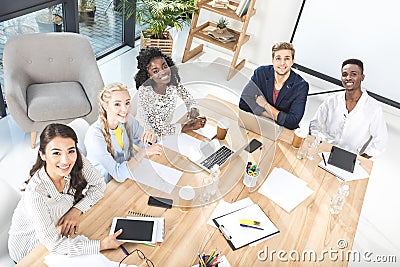 high angle view of multicultural group of business people looking at camera while sitting at table Stock Photo