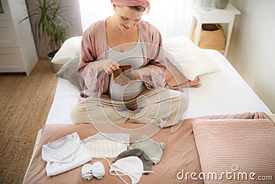 High angle view of pregnant woman looking at little clothes for her baby, packing them to maternity ward. Stock Photo