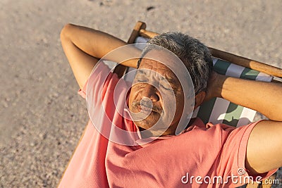 High angle view of retired senior biracial man sleeping with hands behind head on chair at beach Stock Photo