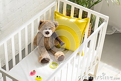 high angle view of teddy bear, other toys and yellow pillow in baby crib Stock Photo