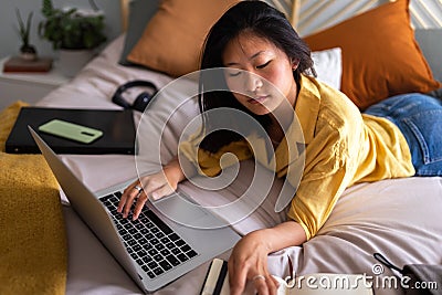 High angle view of teenage asian girl doing homework at home using laptop. Chinese teen female studying in bedroom. Stock Photo