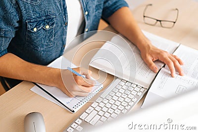 High-angle view of unrecognizable male student studying online from home using computer, writing notes, watching video Stock Photo