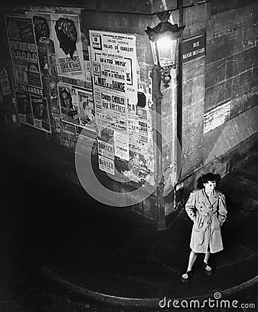 High angle view of a young woman waiting next to a lantern on a dark street corner Editorial Stock Photo