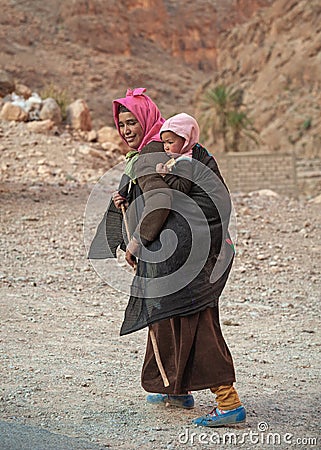 HIGH ATLAS / MOROCCO- MARCH 6, 2014: Young poor Moroccan woman with a child walks away Editorial Stock Photo
