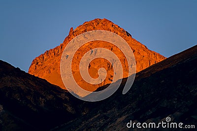 High desert peak illuminated by the golden light of sunset above a ridge that is in shadow Stock Photo