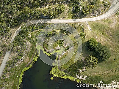 High drone aerial down onto lines formed by pipes, a road, the plant lined waters edge, and power lines Stock Photo