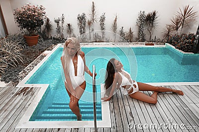 High fashion two bikini models with sexy body in white swimwear posing by swimming pool at luxurious villa. Glamour Portrait of Stock Photo