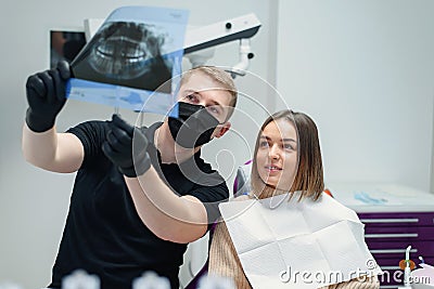 High-qualified dentist shows the young female patient an X-ray of the teeth in the dental chair at modern clinic. Stock Photo