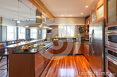 High quality contemporary home kitchen with wood cabinets, hardwood floor, stainless steel appliances, windows and accent lighting Stock Photo