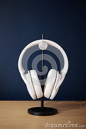 White wireless head large headphones stand on a wooden table on a black stand on a blue background side view Stock Photo