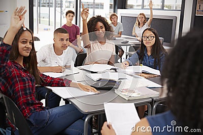 High school kids raise hands, teacher sitting at their desk Stock Photo