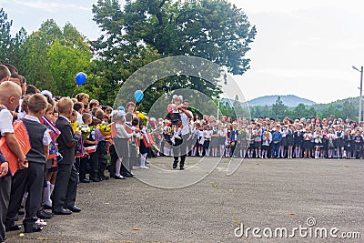 High school student with a first grader in her arms and other schoolchildren in the schoolyard at the grand opening of the school Editorial Stock Photo