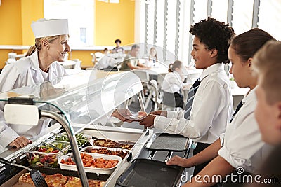 High School Students Wearing Uniform Being Served Food In Canteen Stock Photo