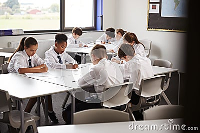 High School Students Wearing Uniform Sitting And Working Around Table In Lesson Stock Photo