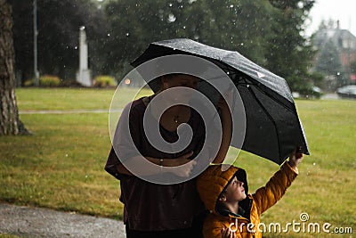 Young woman and little boy using a black umbrella for shelter under rain Stock Photo