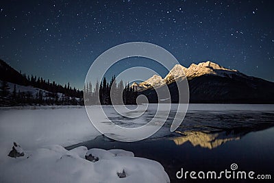 High snow covered mountain, in full moon light with a half frozen lake under night sky full of stars, Banff national Park, Canada Stock Photo