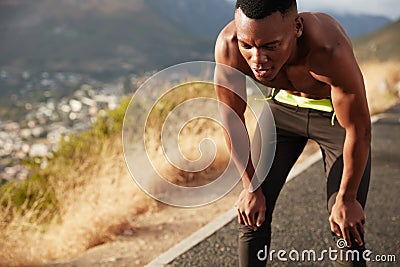 High speed athletic man with healthy dark skin, jogges oiutside city, catches breath, feels tired of exhausting Stock Photo