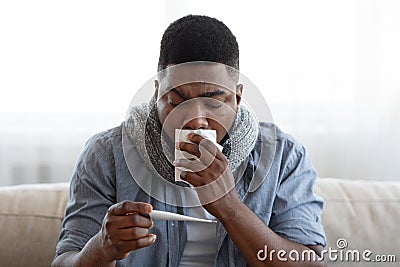 High Temperature. Sick quarantined man sitting with thermometer in hands at home Stock Photo