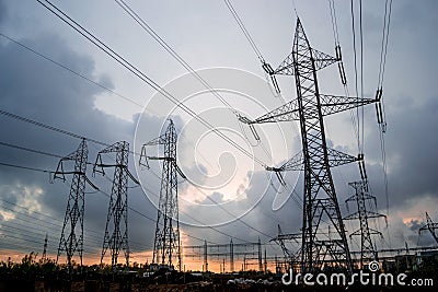 High-voltage electricity grid of power lines, with stormy clouds breaking apart at sunset. Electric transmission towers. Stock Photo