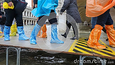 high water in Venice in Italy and people walking over the walkways in waterproof gaiters Stock Photo