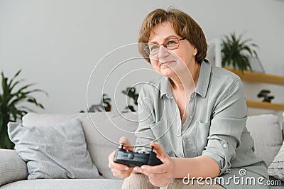 A highly emotional older lady sits on the couch at home and plays video games. Grandma wins while sitting alone at home. Stock Photo