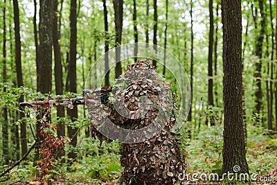 A highly skilled elite sniper, camouflaged in the dense forest, stealthily maneuvers through dangerous woodland terrain Stock Photo
