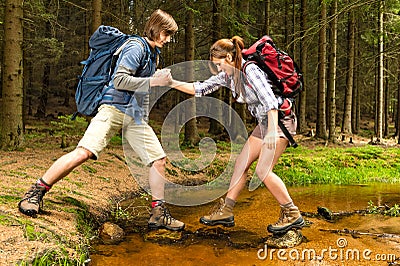 Hiker boy help trekking girl crossing creek Stock Photo