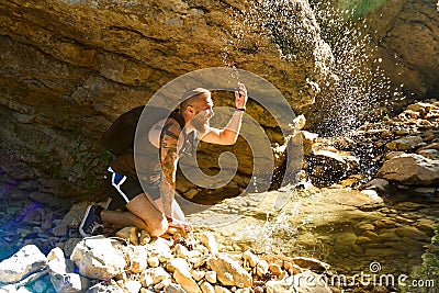 Hiker drinking water from the river. Man enjoys clean fresh unpolluted water in the mountain creek Stock Photo
