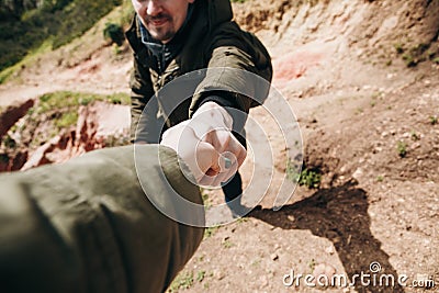 A hiker gives a hand to another person during hiking in a mountainous area. Stock Photo