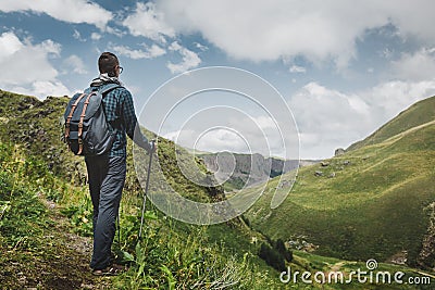 Hiker Man With Backpack And Trekking Poles Resting And Looking At The Mountains In Summer Outdoor, Rear View Stock Photo