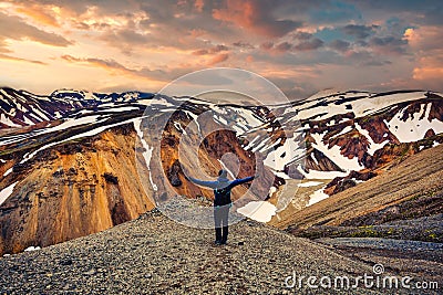 Hiker man standing with arms raised on the cliff with volcanic mountain and snow covered from Blanhjukur trail on summer in the Stock Photo