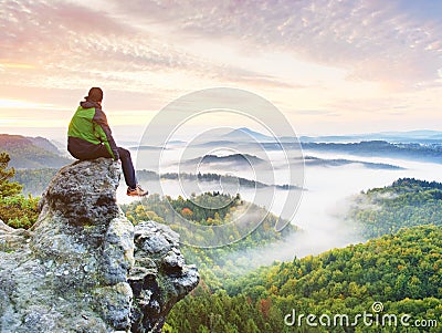 Hiker man take a rest on mountain peak. Man sit on sharp summit and enjoy spectacular view. Stock Photo